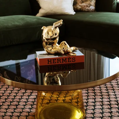 Golden sculpture on Hermès book atop a glass table, with a green sofa in the background.