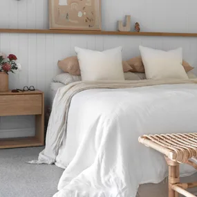 Cozy bedroom with a white bedspread, wooden nightstand, flowers, glasses, and minimal decor.