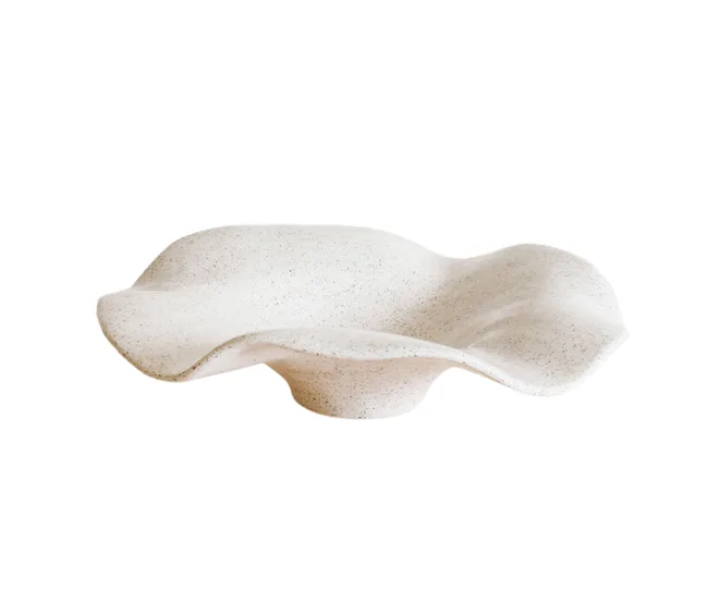 Wavy, speckled white ceramic bowl with an organic shape on a white background.