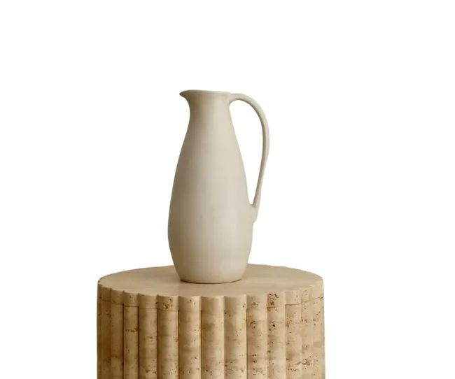 White ceramic jug on a textured, cylindrical wooden stool against a plain background.