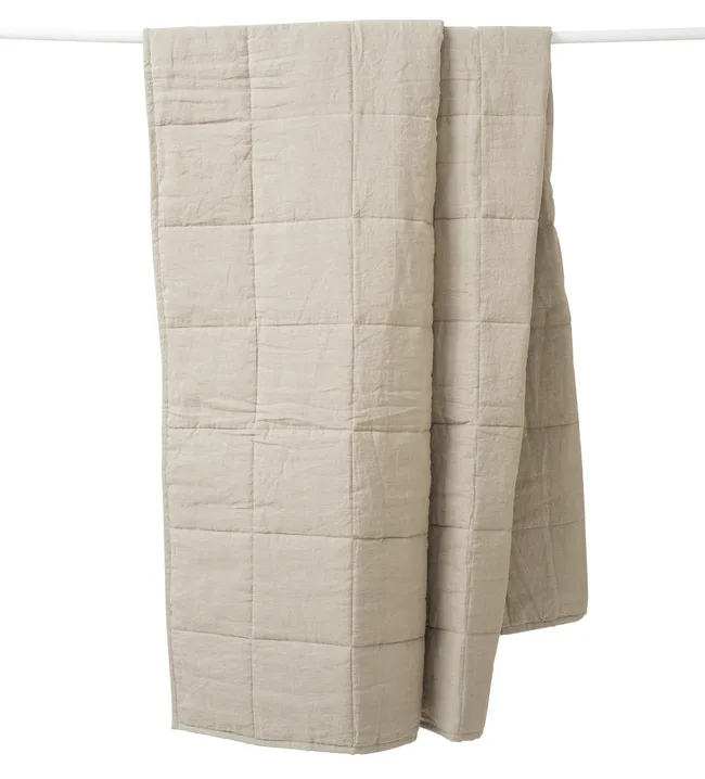 Beige quilted blanket hanging over a rod, showcasing a simple grid pattern.