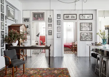 Stylish room with art-filled walls, dark wooden floors, a patterned rug, decorative furniture, and natural light.