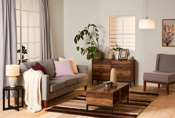 Cozy living room with a gray sofa, wooden furniture, plants, and soft lighting.