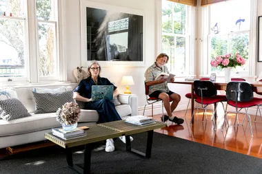 Two people relaxing at home; a woman with a laptop on the sofa and a man reading at the table.