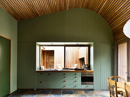Olive green kitchen with vaulted wood ceiling, built-in cabinets, and a large window overlooking an outdoor space.