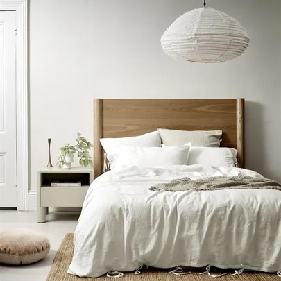 Wooden bed with white bedding, a nightstand with a plant, and a hanging paper lantern in a minimalist bedroom.
