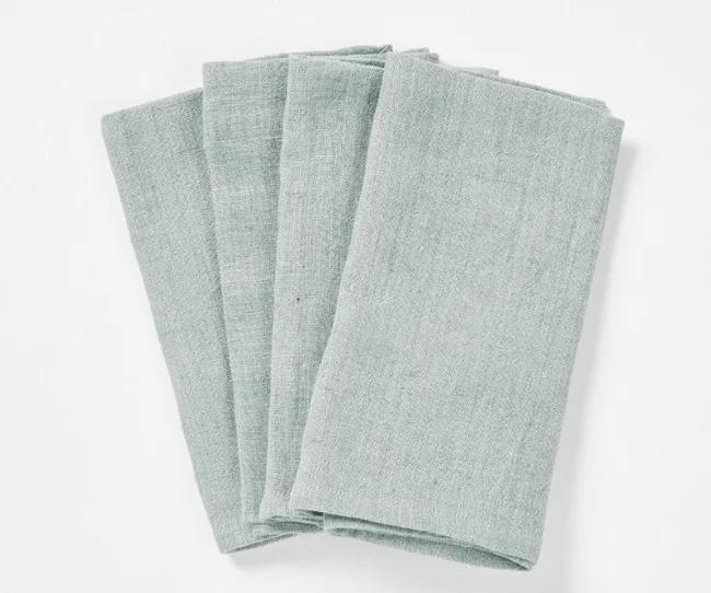 Four folded light gray cloth napkins stacked on a white surface.