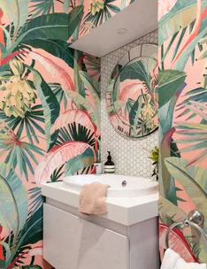 Bathroom with vibrant tropical wallpaper, round mirror, hexagonal tile backsplash, and white vanity with towel.