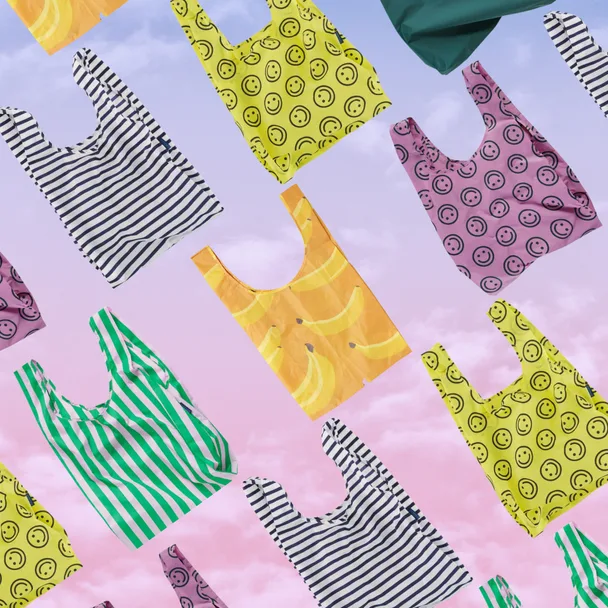 Colorful reusable bags with stripes, smiley faces, and banana designs on a pastel sky background.