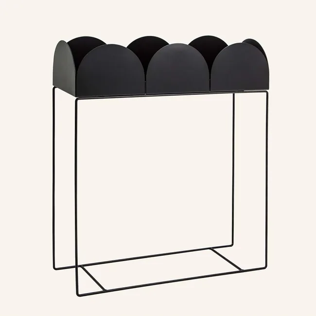 Black metal magazine holder with a scalloped design on a minimal wireframe stand.