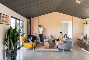 A family of four sits on couches in a modern living room with plants and a dog.
