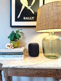 Marble table with a stack of books, a plant, a speaker, a glass lamp, and a vintage Bally poster on the wall.