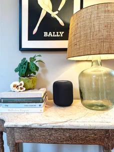 Marble table with a stack of books, a plant, a speaker, a glass lamp, and a vintage Bally poster on the wall.
