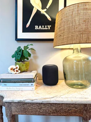 Marble table with a stack of books, a plant, a speaker, a glass lamp, and a vintage Bally poster on the wall.