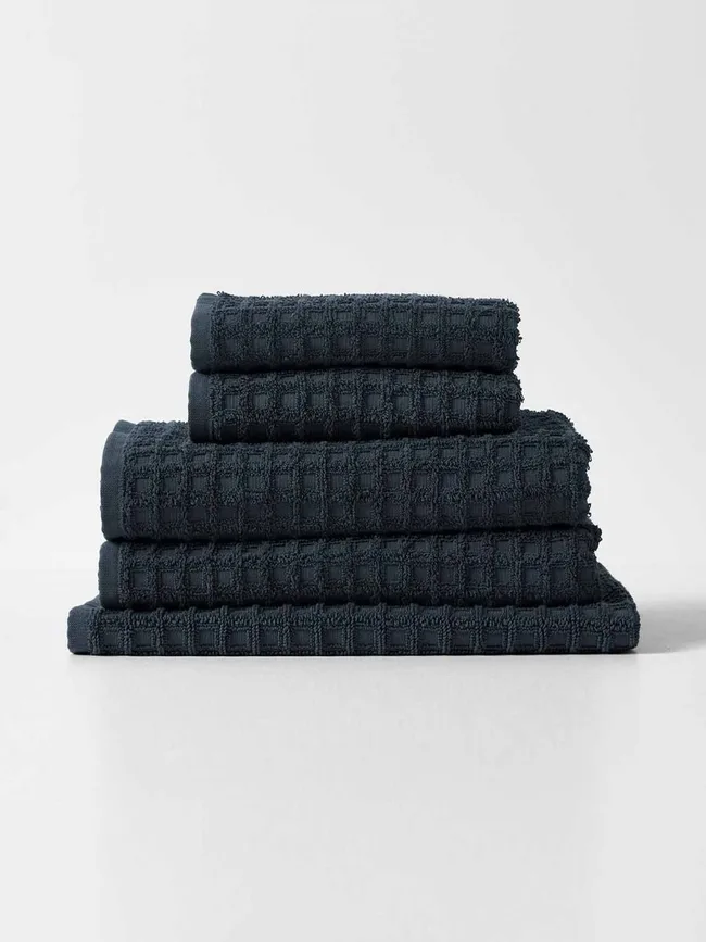 Stack of dark waffle-textured towels on a plain surface.