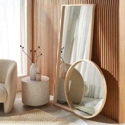 Modern room with wooden paneling, a round and a tall mirror, a textured chair, round table, and decorative vases.