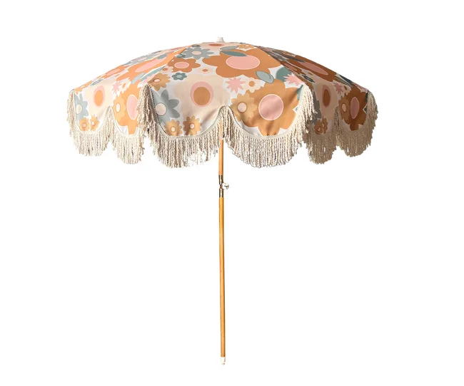 Retro-style beach umbrella with floral patterns and fringed edges on a wooden pole.