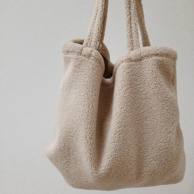 Beige, textured sherpa tote bag with soft handles, hanging against a plain white background.