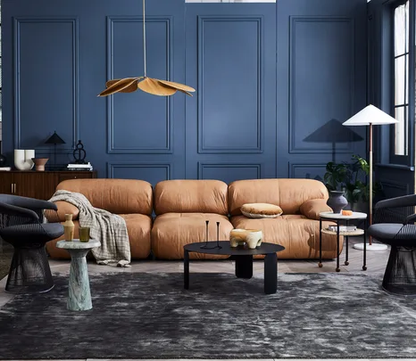 Tan leather sofa, blue paneled walls, modern lighting, black coffee table, and decorative items in a stylish living room.