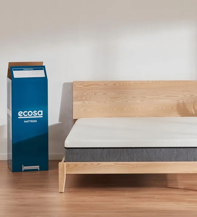 Natural wood bed frame with a white mattress and a blue Ecosa mattress box on a wooden floor.