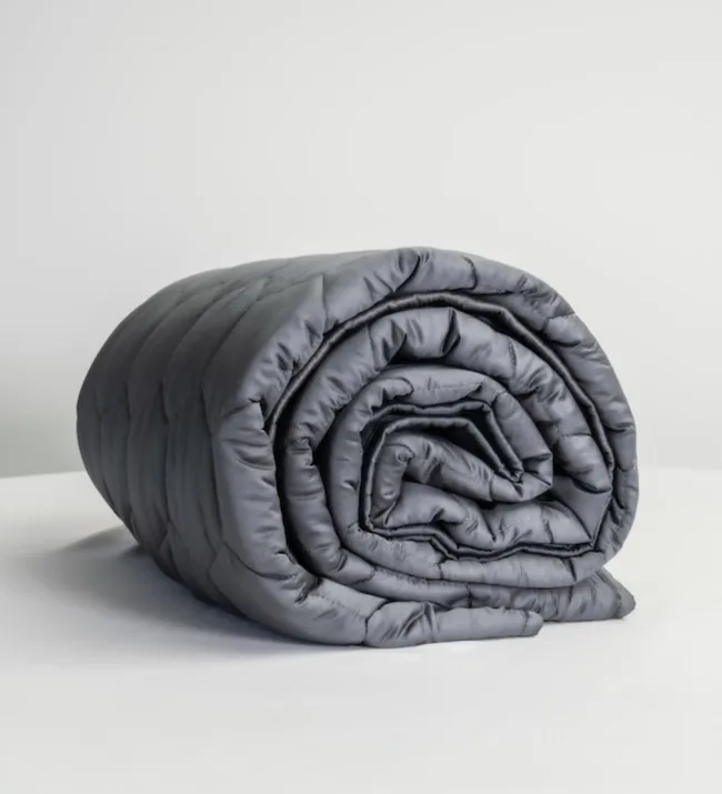 Rolled-up gray weighted blanket on a white surface, against a plain background.