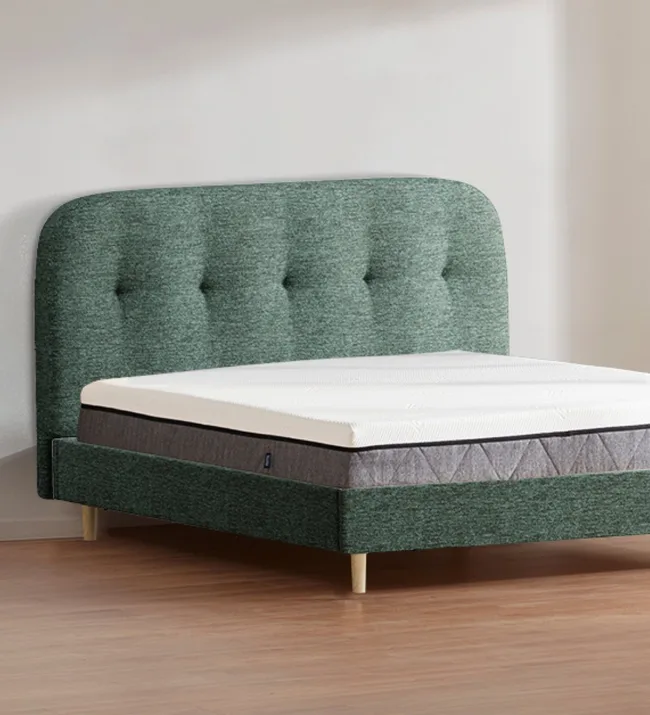 Green upholstered bed with tufted headboard and mattress on wooden floor.