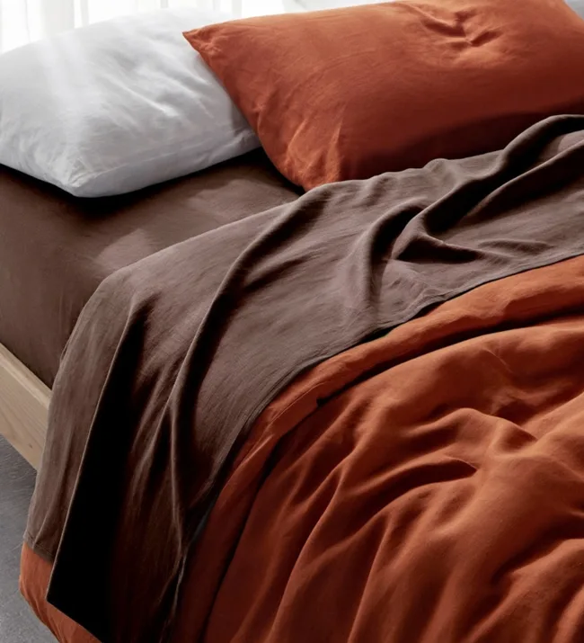 Brown and rust-colored bedsheets with a white pillow on a bed.