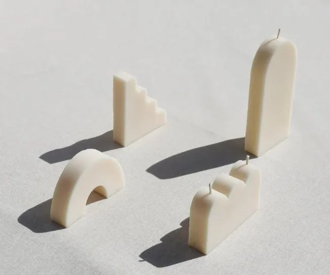 Unique white candles in various geometric shapes on a light surface with shadows.