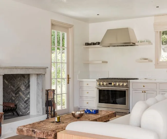 Living room with rustic wooden coffee table, modern fireplace, and a minimalist kitchen with a stove and metal range hood.
