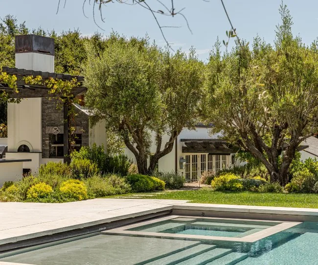 Modern home surrounded by trees and greenery, featuring a swimming pool in the foreground.