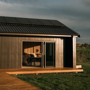 Modern tiny home exterior with solar panels, open sliding door revealing bedroom interior at sunset.