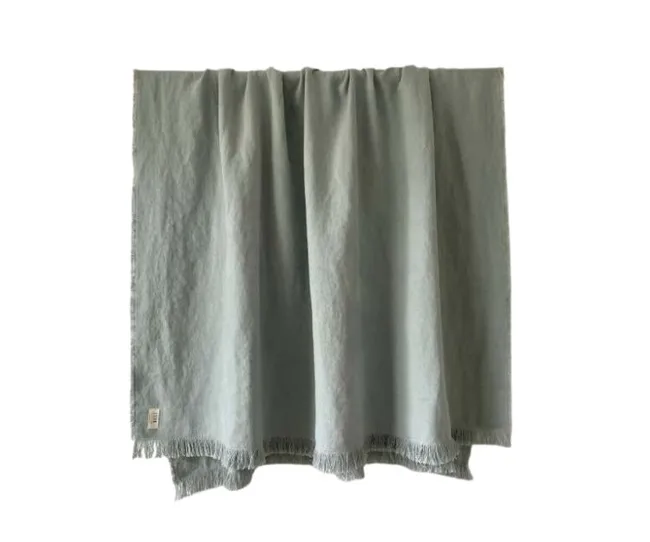 A light green throw with fringed edges hanging vertically against a plain background.