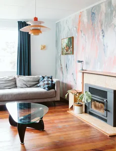 Cozy living room with a gray sofa, abstract wall art, mid-century lamp, glass coffee table, and wood floor.