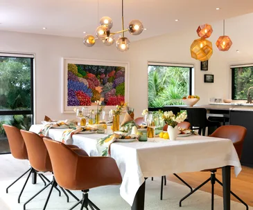 Dining room with modern chandelier, artwork, brown chairs, and a table set for a meal with flowers and candles.