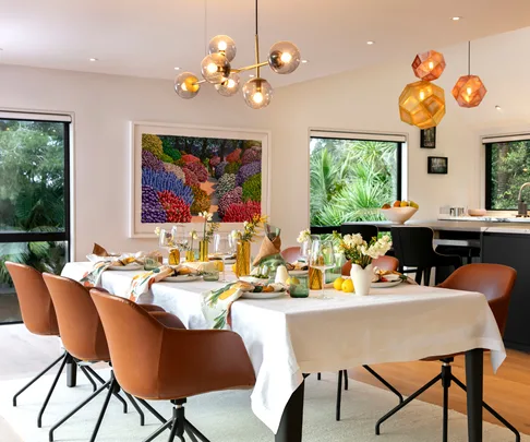 Dining room with modern chandelier, artwork, brown chairs, and a table set for a meal with flowers and candles.