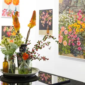 Flower arrangement in glass bottles on a round tray, with colorful floral paintings in the background.