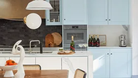 A kitchen painted light blue with a white pendant light, champagne on the bench and a coffee machine.