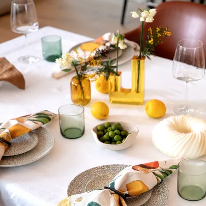 Elegant table setting with vibrant napkins, glasses, lemons, green olives, and floral centerpieces on a white cloth.
