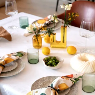 Elegant table setting with vibrant napkins, glasses, lemons, green olives, and floral centerpieces on a white cloth.