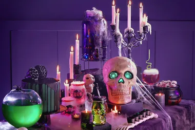 Halloween-themed table with glowing skull, candles, cobwebs, cauldron, and spooky decorations.