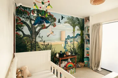Children's room with a nature-themed mural, crib, toys, books, and hanging mobile.