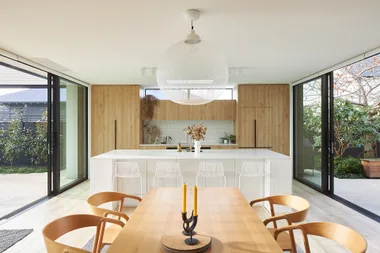 Modern kitchen and dining area with wooden cabinets, large island, pendant light, and sliding glass doors to a garden.