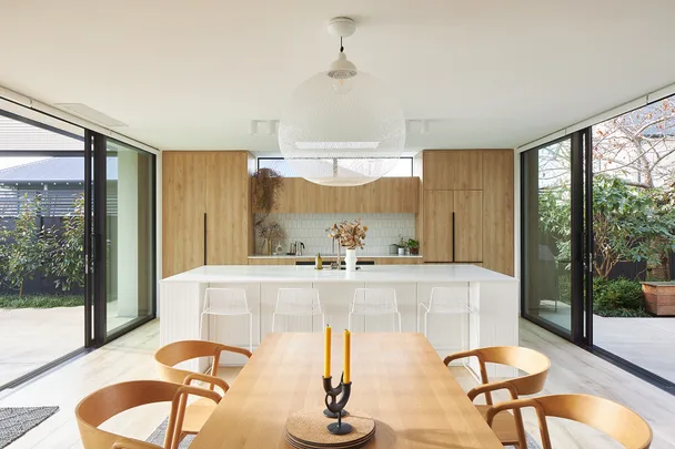 Modern kitchen and dining area with wooden cabinets, large island, pendant light, and sliding glass doors to a garden.