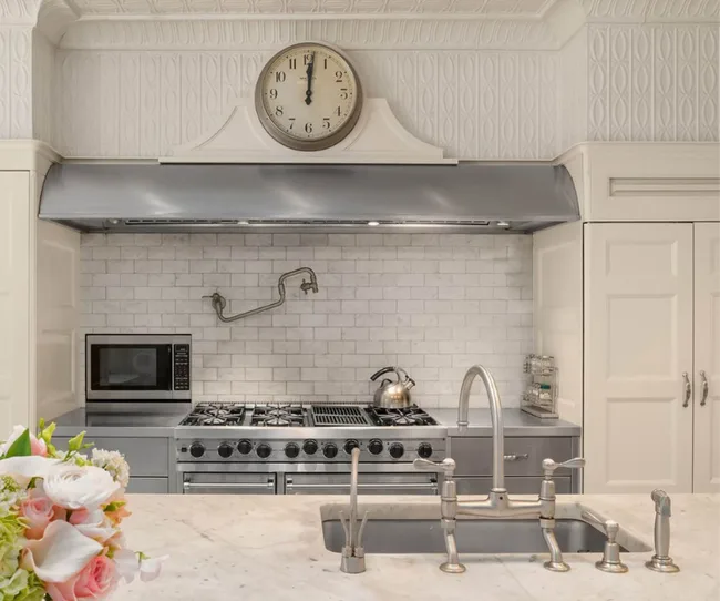 Elegant kitchen with a stainless steel stove, microwave, and kettle, marble countertops, and a decorative wall clock.