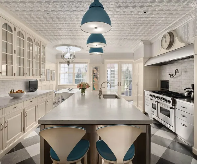 Luxurious kitchen with marble island, blue pendant lights, classic cabinetry, and large range stove.