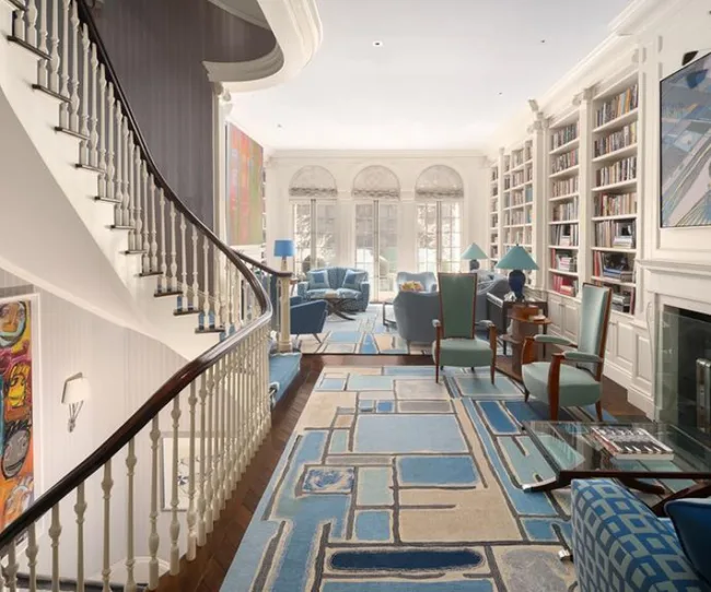 Elegant living room with spiral staircase, blue-themed seating, large windows, and floor-to-ceiling bookshelves.