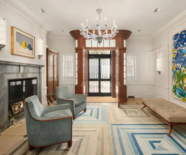 Luxurious room with a fireplace, two chairs, abstract paintings, elegant chandelier, and plush bench.