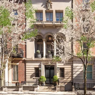 Elegant townhouse facade with arched windows and spring trees in bloom, creating a picturesque urban scene.