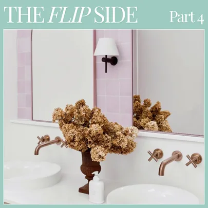 Bathroom with dual sinks, wall-mounted faucets, and a mirror reflecting dried flowers in a vase, under a light fixture.