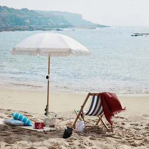 Beach scene with an umbrella, deck chair, and blanket by the sea. Perfect for a relaxing day by the ocean.